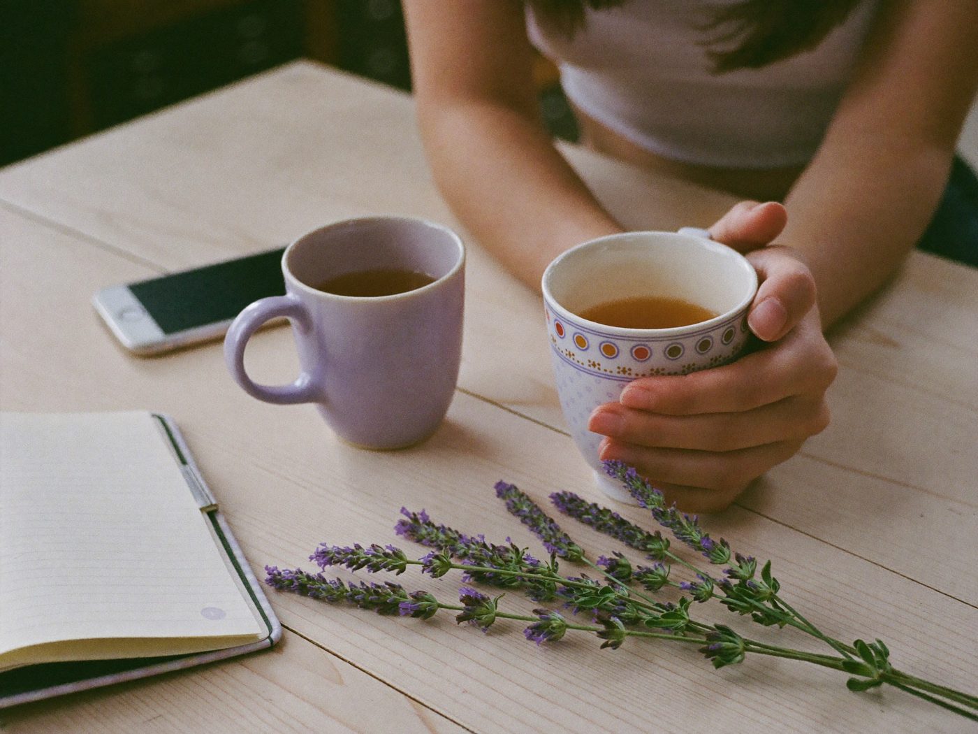 Hands around a mug of tea next to a sprig of lavender and a notebook